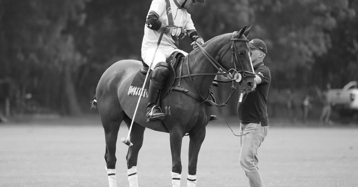 Foto en blanco y negro de un jugador de polo a caballo con el entrenador en el campo.