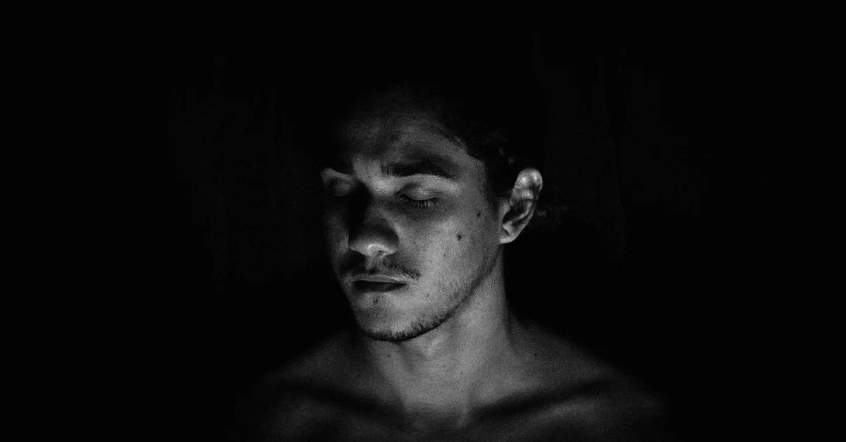 Retrato en blanco y negro de un hombre sin camisa con los ojos cerrados, evocando contemplación.