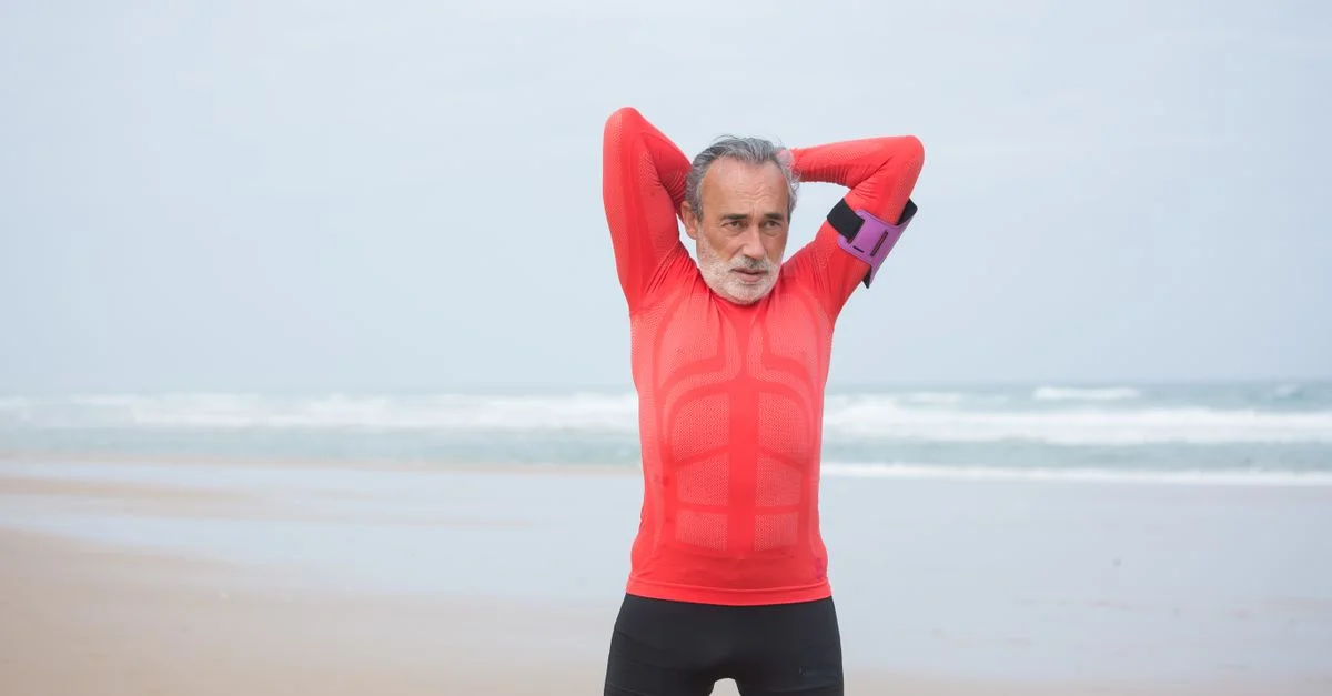 Hombre anciano en ropa deportiva roja estirándose en una serena playa portuguesa.
