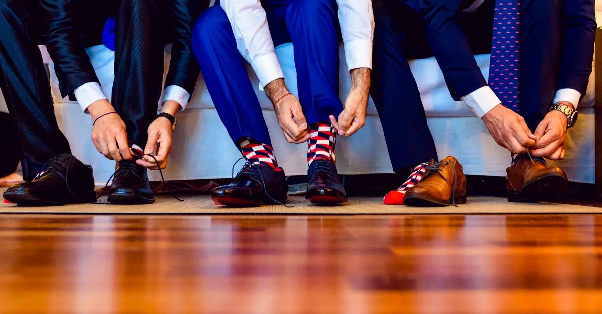 Hombres en trajes formales atándose los zapatos de cuero, capturados en interiores.